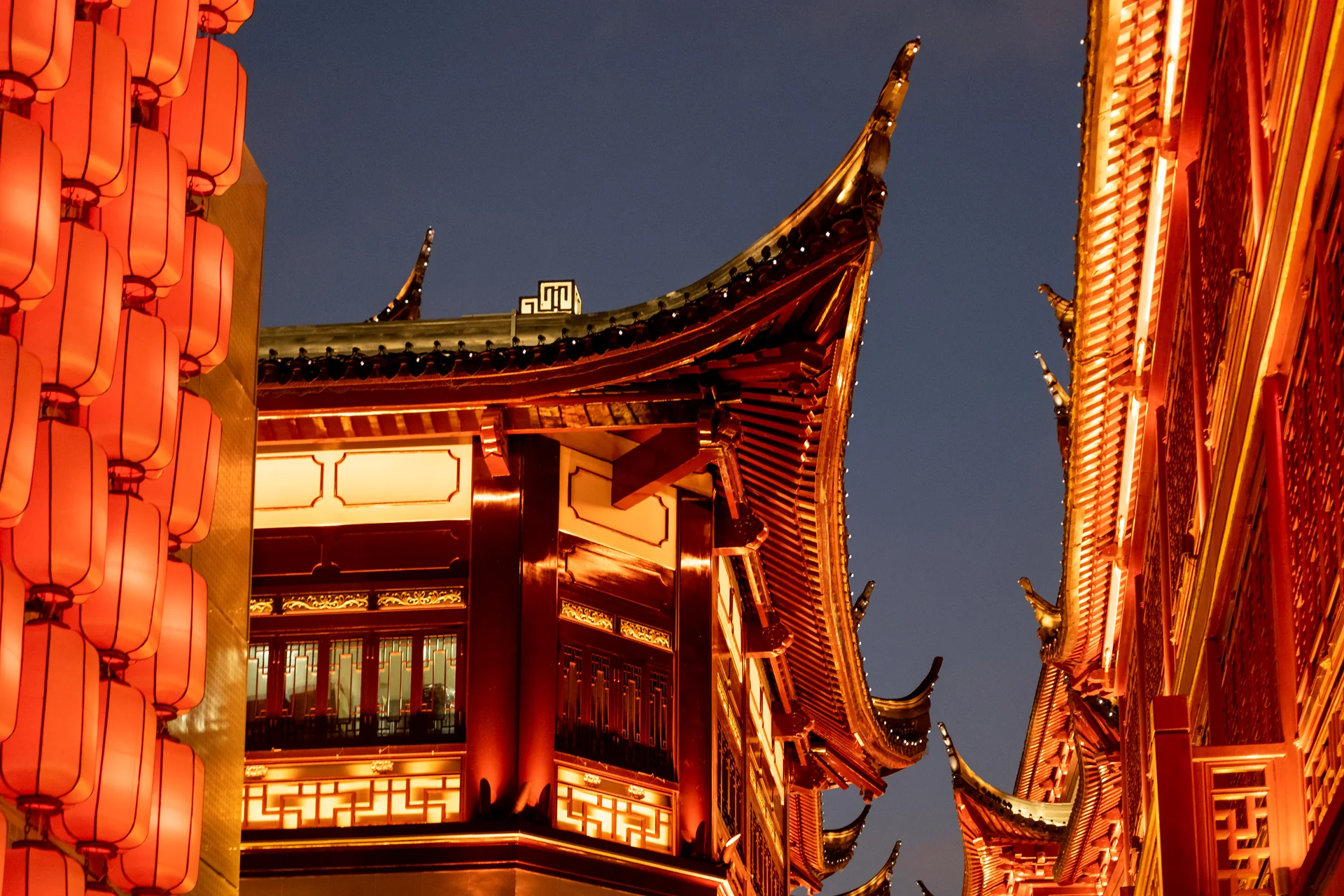 Rote Laternen und die beleuchteten, geschwungenen Dachvorsprünge eines traditionellen chinesischen Gebäudes in Shanghai bei Nacht